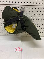 Side view of dog coat showing olive green water resistant outer fabric, yellow fleece lining, and attached black harness straps with metal D-ring ring for leash.