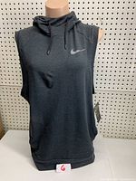 Front view of the men's medium dark gray sleeveless Nike workout hoodie on a mannequin, showing the front Nike swoosh logo and hood with drawstrings, in new condition with tags attached.