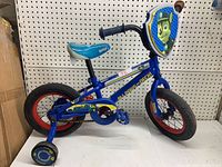 Side view of blue Paw Patrol boys bike with training wheels, showing tire size and front Paw Patrol character shield.