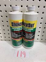 Two bottles of Ultra Stains R Out stain remover side by side against a pegboard background.