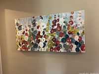 Front angled view of the rectangular canvas painting showing abstract circular floral designs in blue, red, white, and green colors on a pale background.