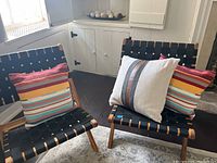 Two chairs showing colorful striped woven pillow and neutral beige pillow with leatherlook stripe accent.