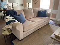 Front view of the light beige microfiber couch with three seat cushions and back cushions, decorated with blue pillows and a striped throw blanket.