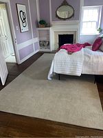 Full view of cream colored area rug in bedroom placing near bed and fireplace with hardwood floor visible.