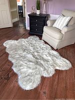 Rug displayed next to beige armchair and black three-drawer nightstand on brown wood floor