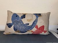 Front view of the rectangular throw pillow with embroidered blue and red koi fish design on beige fabric.