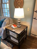Full view showing the table next to a sofa, a table lamp on top,and storage bins on shelves.