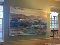 Front view of the large abstract canvas painting with white frame hung on a light blue wall, illuminating the range of blues, beiges, and rust colors.