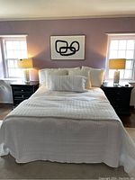 White bedding set arranged on bed with two black nightstands and lamps in a purple-walled room