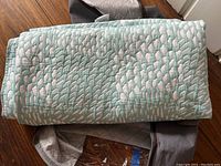 Quilt and shams folded and stacked on wooden surface, showing spa green and white pattern.