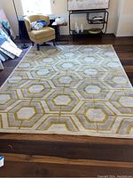 Full view of the rectangular rug on wood floor near a chair and shelves showing overall pattern and size.