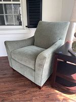 Front left angle view of sage green chenille armchair showing armrests, cushioned seat and wooden legs.