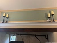 Four hammered metal candlesticks displayed on a ledge against a pale green wall, each holding a cream pillar candle. Varying heights, arranged with two taller and two shorter candlesticks.