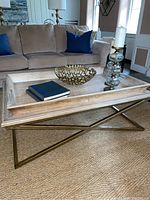 Full view of the modern tray style coffee table with removable wooden tray top and brass-toned X-shaped legs in a living room setting.
