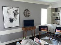 Wide shot of large canvas wall art of a white horse and a small TV on wooden stand in a living room corner