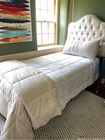 Single bed made with white lightweight comforter, white king-sized pillow with cover, in a green room.