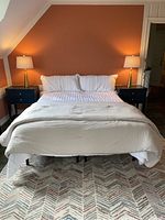Full view of king bed with white quilted comforter and two king pillows against a brown wall with black nightstands and lamps on each side.