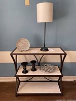 Full view of console table with white lamp, decorative plate, black candle holders, and silver tray on shelves.