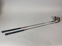 Two PING wedges placed side by side showing full length from grip to club head.