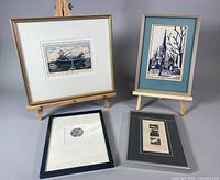 Three framed prints displayed on small wooden easels and flat surfaces, showing front of all artworks and frame conditions.