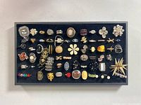 Full tray view of assorted costume rings with various styles including pearl clusters, geometric and floral designs