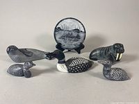 Photo showing five small carved animal sculptures and one etched round wall art piece displayed on black stand.