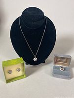 Overview of the jewelry set including necklace on display bust, stud earrings in green box, and ring in grey velvet box.