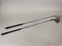 Two golf wedges laid flat showing the full clubs with grips and heads, one with minor wear and clean chrome shaft (Callaway), one showing oxidized clubface (Titleist).