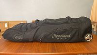 Side view of black Cleveland Golf travel bag showing padded sections and wheels