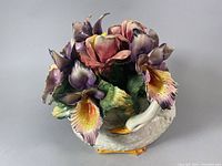 Porcelain floral arrangement depicting large colorful flowers in a white swan-shaped base with detailed petals and leaves.