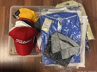 All hats and shirts in plastic bin on wood floor.