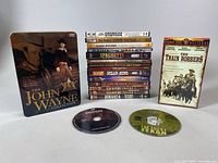 Full view of Western DVDs including John Wayne Collection metal case, The Train Robbers DVD, and multiple other Western DVD titles stacked.