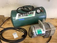 Air compressor tank with hose and motor on wooden surface. Shows Speedaire branding and equipment layout.