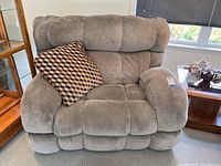Front view of oversized power recliner with patterned throw pillow on the left armrest, placed indoors near windows.
