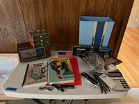 Full overview of all items on table including clock radio, books, pens, cutters, puncher, calculator, organizer box, and trash can.