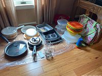 Wide view of lot items on floor including pans, bakeware, baking trays, Tupperware, insulated totes, measuring cup.