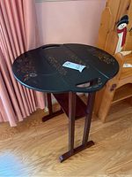 Full view of the black round drop leaf table with floral stencil on top and legs visible.