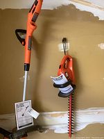 Photo showing the Black & Decker electric hedge trimmer with manual, and the electric edger hung on the wall against a garage wall background.