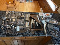 Overview of flatware laid out on table including forks, spoons, knives, serving utensils, and wooden cutlery box.