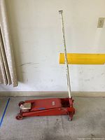 Full view of red Dayton 2-ton hydraulic floor jack with long white handle, showing general condition including surface rust and scratches.