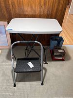 Front view showing folding table with white top and step stool in front