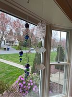 Photo showing two hanging sun catching mobiles near a window, one with glass orbs and wire spirals and the other with pink textured glass and iridescent squares.