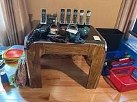Square table with tinted glass top. Features thick wooden legs and a metal trim edge. Table surrounded by various household items, which are not included.