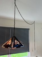 Full view of hexagon stained glass hanging lamp lit, showing floral panels, hanging chain and window background