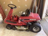 Side view of red Honda riding mower model 3011, showing mower deck, tires, steering wheel, and extra blades placed on top.