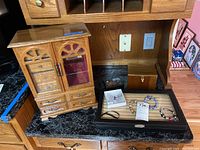 Overall view of wooden jewelry cabinet, glass box, wooden box, tissue case, bracelets, and pin taken on countertop.