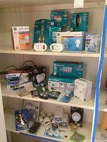 Shelf with multiple light bulbs in boxes including LED soft white, EcoSmart brand LED and CFL bulbs, decorative bulbs, and Philips packaging. Two white digital timer units placed on shelf.