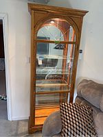 Full view of tall wooden display cabinet with glass door and sides, showing interior glass shelves and interior light on.