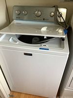 Front view of the white Maytag top load washer with open lid showing control panel and inside tub.
