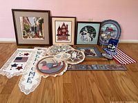 Photo showing all needlework and tapestry pieces laid out on floor, including framed and unframed items with patriotic themes